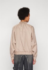 Veste bomber beige clair en tissu lisse, dotée d'une taille et d'un col froncés. Le design comprend des coutures discrètes et une coupe décontractée.