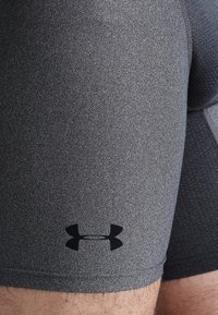 Pantaloni sportivi grigi realizzati in tessuto testurizzato, con una vestibilità aderente e un logo nero sul lato sinistro in basso.