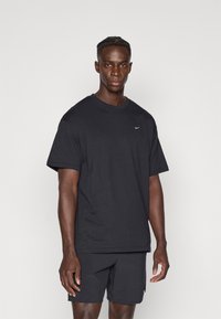 Μαύρο t-shirt Nike με χαλαρή εφαρμογή και κοντά μανίκια, παρουσιασμένο με ταιριαστά μαύρα σορτς, με μικρό λογότυπο στο στήθος.