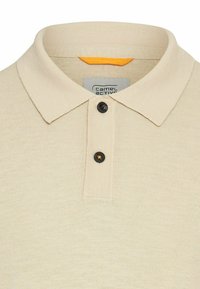 Beige polo shirt lavet af strikket stof, med en klassisk krave, tre knapper i sort og med en orange detalje indeni kraven.