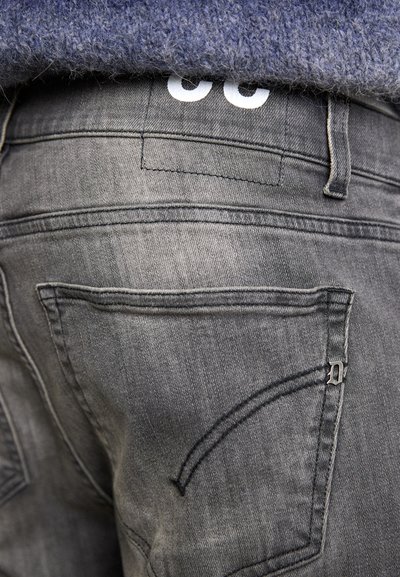 Grå denimjeans med en glatt tekstur, som har to baklommer og en unik sømdetalj, komplementert av en hvit logo på livet.