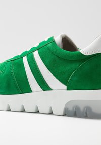 Sneaker verde in suede con dettagli bianchi, con una suola bianca spessa con motivi a onda e una cavigliera imbottita per il comfort.