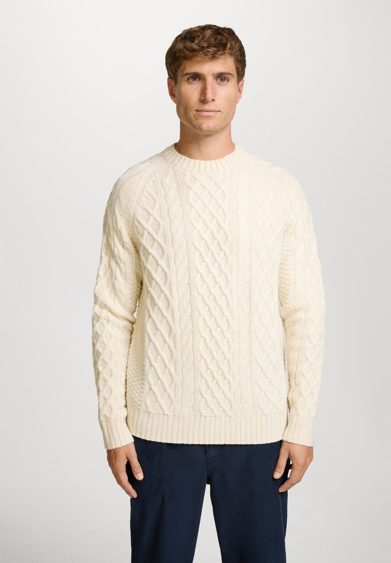 Helles, cremefarbenes Grobstrickpullover mit geripptem Kragen und Saum, ausgestattet mit strukturierten Mustern und einem lockeren Schnitt.