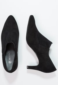Chaussures à talons en daim noir avec un bout pointu, des côtés découpés et un talon fin et structuré. Présente une doublure intérieure lisse et des détails de coutures subtils.