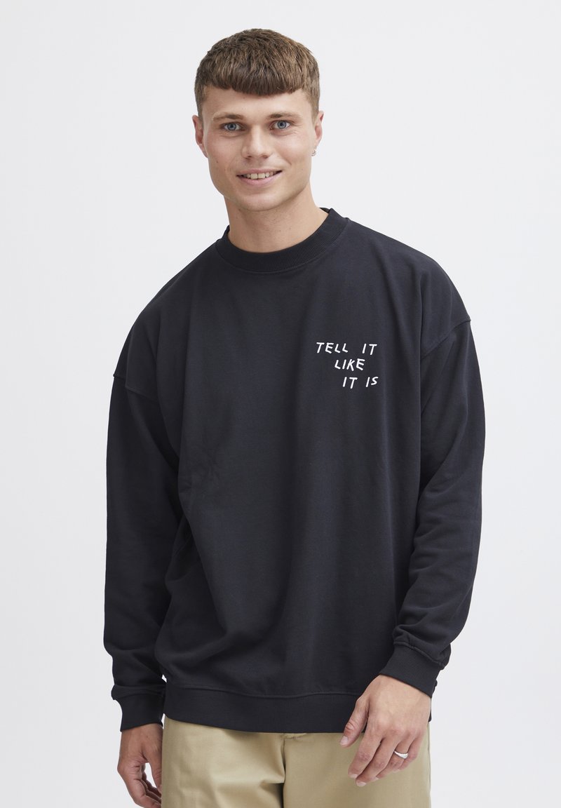 Black sweatshirt with long sleeves, ribbed crew neck, featuring white text "TELL IT LIKE IT IS" on the front. Soft fabric, relaxed fit.