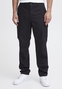 Sorte cargo bukser med en afslappet pasform, der har dobbelte sidelommer, en glat tekstur og en knaplukning i taljen. Sammen med hvide sneakers.