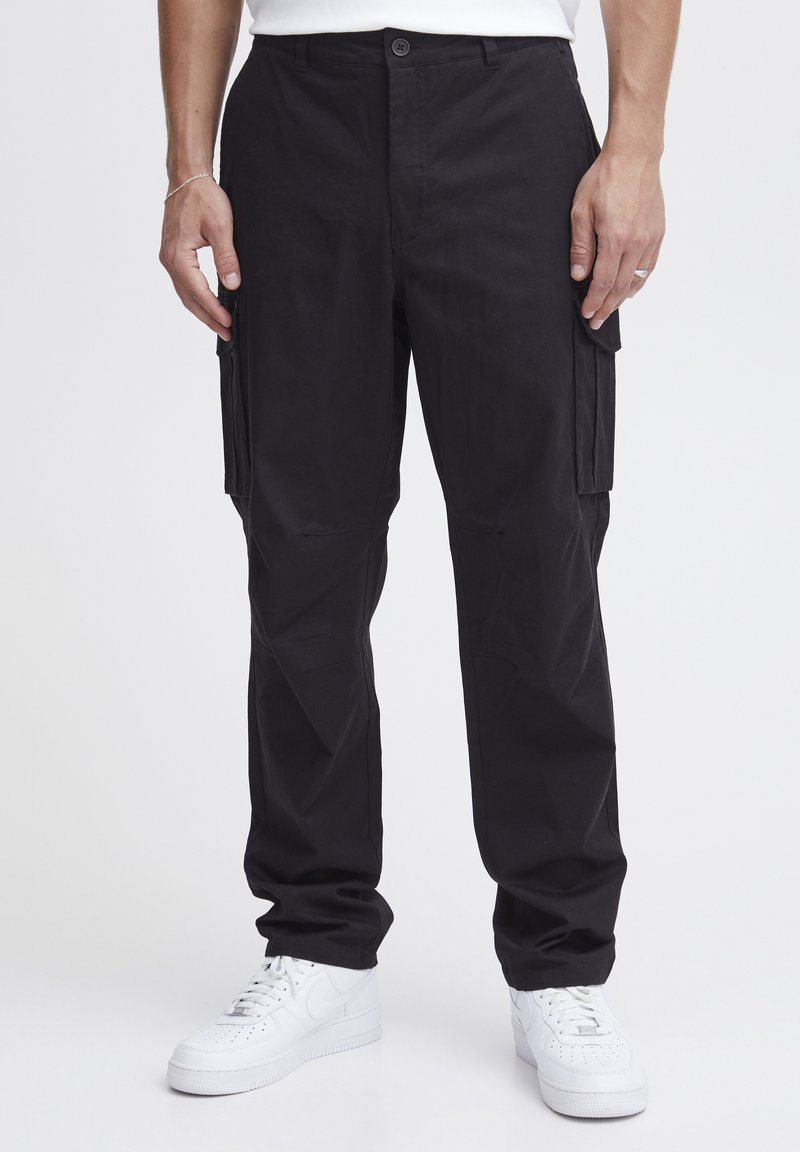 Sorte cargo bukser med en afslappet pasform, der har dobbelte sidelommer, en glat tekstur og en knaplukning i taljen. Sammen med hvide sneakers.