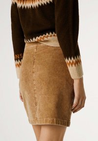 Gonna mini in corduroy marrone con una silhouette aderente, caratterizzata da una texture sottile e un orlo che termina a metà coscia, abbinata a un maglione lavorato a maglia.