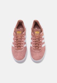 Ténis de camurça rosa com riscas brancas, área de atacadores texturizada e colarinho acolchoado. Logótipo amarelo na lingueta, sola de borracha branca minimalista.