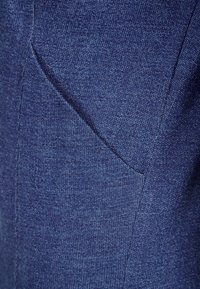 Mörkblått tyg med en strukturerad yta. Har en diagonal ficka sydd på sidan, med ett subtilt blandat mönster.