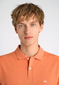Polo arancione realizzato in tessuto texturizzato, con colletto a due bottoni, maniche corte e un piccolo logo bianco sul petto.