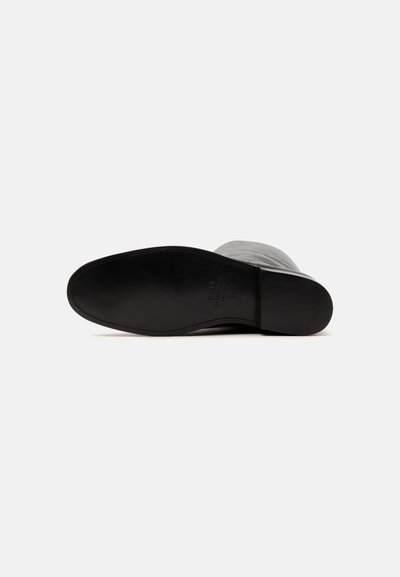 Semelle en cuir noire d'une botte grise à la cheville vue par le dessous sur un fond blanc uni.