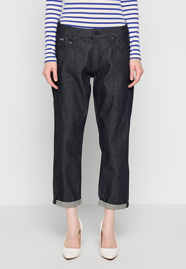 Jean en denim foncé avec une coupe décontractée, des poignets retroussés et un design classique à cinq poches. Associé à un haut à rayures bleues et blanches à manches longues.