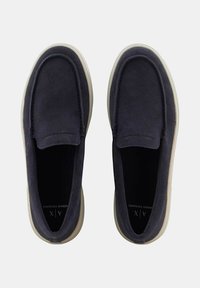 Scarpe slip-on in suede blu navy con una texture liscia, punta rotonda e suola in gomma di colore chiaro a contrasto. Design minimalista senza hardware visibile.
