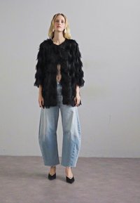 Melns mākslīgās kažokādas mētelis ar relaksētu piegriezumu, atvērtu priekšu un trīs ceturtdaļu piedurknēm, apvienots ar gaiši ziliem augstās jostasvietas platām biksēm un melnām augstpapēžu kurpēm.