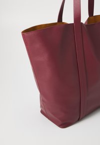 Dark burgundy leather tote bag with a smooth texture, contrasting yellow interior, and two vertical seams. Double flat handles.
