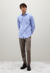 Camicia azzurra chiara con bottoni e maniche lunghe, accompagnata da pantaloni beige e scarpe nere. Tessuto liscio, design aderente e senza motivi visibili.