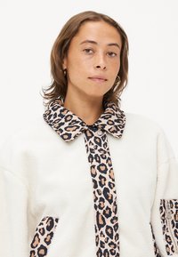 Witte fleece jack met een kraag en voorplacket in luipaardprint, voorzien van twee met rits sluitbare zijzakken en een zachte, gestructureerde afwerking.