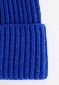 Sininen neulottu pipo, joka on valmistettu tekstuurilangasta. Pipossa on ribattu muotoilu, joka korostaa pystysuoria viivoja, ja alareunassa on taitettu reuna.