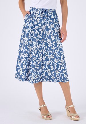 Jupe midi bleue à motif floral blanc, taille élastique avec cordon, portée avec des sandales compensées dorées et un top blanc.