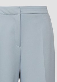 Pantalon bleu clair cintré avec une ceinture plate, une couture latérale et un détail de pli à l'avant sur un fond neutre.