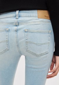 Φωτεινά γαλάζια στενά τζιν από τζιν ύφασμα, με δερμάτινο λογότυπο στη μέση, δύο πίσω τσέπες και διακριτικές ραφές.