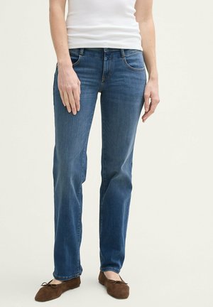Jean en denim bleu avec une coupe droite, présentant cinq poches, un lavage subtil et de légers effet d'usure à l'avant. Associé à des ballerines marron.