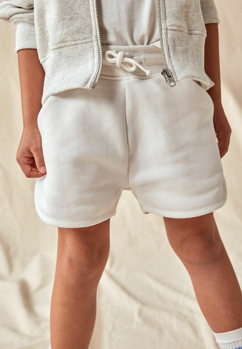 Shorts en coton blancs avec une taille élastique et un cordon de serrage. Comprend des poches latérales et une texture lisse, avec des détails de ourlet arrondi.