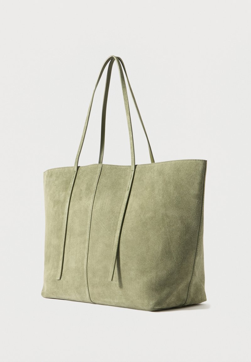 Sac en suede vert avec deux longues poignées, présentant une forme rectangulaire simple et une texture lisse et douce.