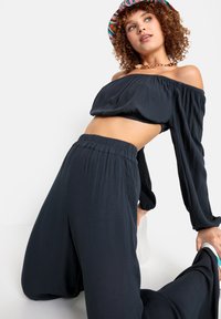 Top corto de color gris oscuro sin hombros con mangas largas, combinado con pantalones de pierna ancha a juego que presentan una tela texturizada.