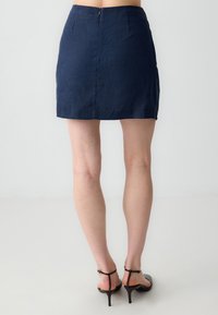 Marineblaue Leinen-Minirock mit geradem Schnitt, ausgestattet mit einem Reißverschluss auf der Rückseite und ohne Taschen, kombiniert mit schwarzen Riemchen-High Heels.