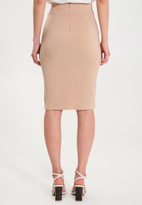 Nudefarbener Bleistiftrock mit tailliertem Design, hoher Taille und einem Reißverschluss hinten. Kombiniert mit weißen Absatzsandalen mit dicken Absätzen.