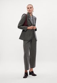 Sivi hounds-tooth sako i odgovarajuće hlače, upareni sa sivom majicom i burbundi kožnom torbom. Sjajne crne cipele s potpeticama upotpunjuju izgled.