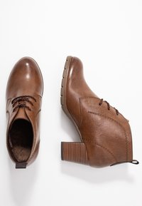 Brązowe botki z syntetycznej skóry, sięgające do kostki, z okrągłym noskiem, sznurowaną detalem, teksturowaną cholewką oraz słupkiem z poziomymi rowkami.