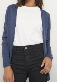 Marineblauer Cardigan aus weichem Stoff, offenes Frontdesign, kombiniert mit einem weißen T-Shirt und schwarzen Jeans. Schlichte, legere Kleidung.