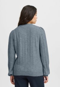 Pilkas megztinis su tekstūra iš briaunų, ilgos rankovės ir apvalus iškirpimas. Pasižymi švelniu paviršiumi ir šiek tiek trumpesniu apvadu.