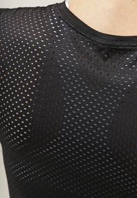 Camisa atlética negra con un diseño de malla que presenta pequeños agujeros distribuidos uniformemente, textura suave y un cuello redondo.