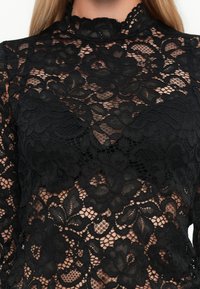Black floral lace high-neck top with sheer sections, covering the upper torso and arms.