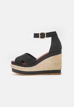 Sort læder kilehæl sandal med krydsede stropper, ankelsnøre og vævet jutebund. Glat tekstur og klart defineret silhuet.