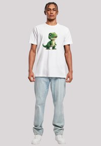 White cotton T-shirt featuring a colorful cartoon dinosaur graphic on the front. Worn with light blue denim jeans and white sneakers.