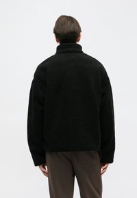 Fekete bolyhos dzseki magas gallérral, textúrált felszínnel és laza szabással. Hosszú ujjakkal és egyenes aljjal tervezték.