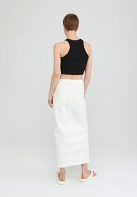 Black cropped tank top, white long denim skirt, smooth texture, minimalistic design; worn with white slip-on shoes, back view.