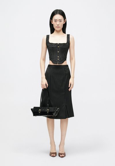 Schwarzes, gestreiftes, kurzes Oberteil mit quadratischem Ausschnitt und Knopfschluss, kombiniert mit einem passenden knielangen Rock. Die Accessoires umfassen eine schwarze Handtasche.