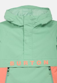 Giacca verde menta con colletto alto, dettagli corallo, grande logo "BURTON" e tasche con zip. Tessuto morbido e leggero.