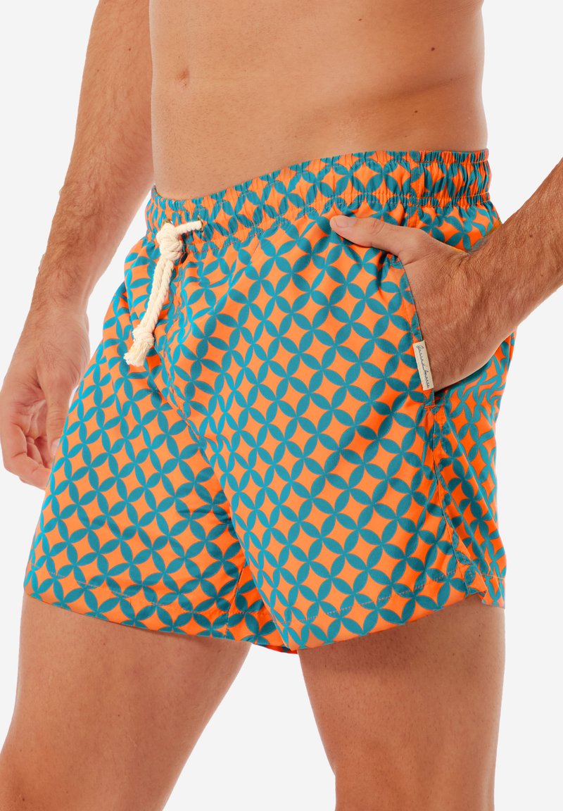 Badeshorts mit elastischem Bund, versehen mit einem geometrischen Muster aus blauen und orangefarbenen Kreisen auf einem türkisfarbenen Hintergrund.