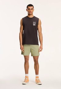 Sort ærmeløs skjorte med frontlomme, oliemarinegrønne shorts og orange høje sneakers. Simpelt, afslappet outfit.