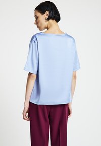 Top in raso azzurro chiaro a maniche corte con vestibilità rilassata e scollo ampio, abbinato a pantaloni larghi color bordeaux. Texture liscia, dettagli minimali.