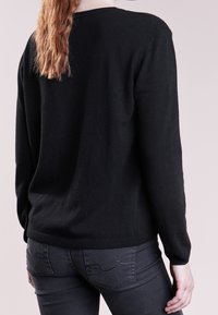 Pull en maille noir avec un col rond, des manches longues et une coupe décontractée. Associé à un jean gris foncé ajusté avec des détails de couture sur les poches.