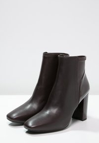 Ciemnobrązowe skórzane botki z blokowym obcasem i bocznymi zamkami błyskawicznymi, umieszczone na białej powierzchni na tle jednolitego tła.