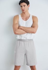 Szare szorty z logo Lacoste po lewej stronie i jasnoszarym pasem w talii. Połączone z białym topem na ramiączkach. Gładka tekstura materiału.